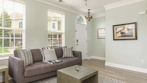 A living room with a grey sofa, patterned throw pillows, a concrete coffee table, a patterned rug, and a framed picture on the wall. - Prime Downtown Cornelius Townhome (Cornelius)