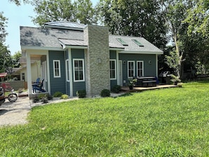 A two-story house with a stone chimney, a porch with chairs, and a grill in the backyard.
