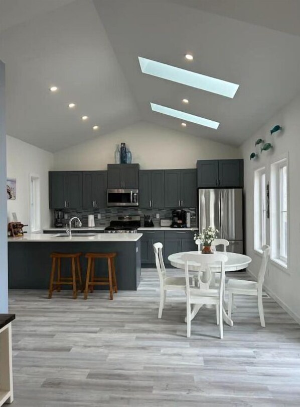 A modern kitchen with dark cabinets, a central island, and a dining area with white chairs.