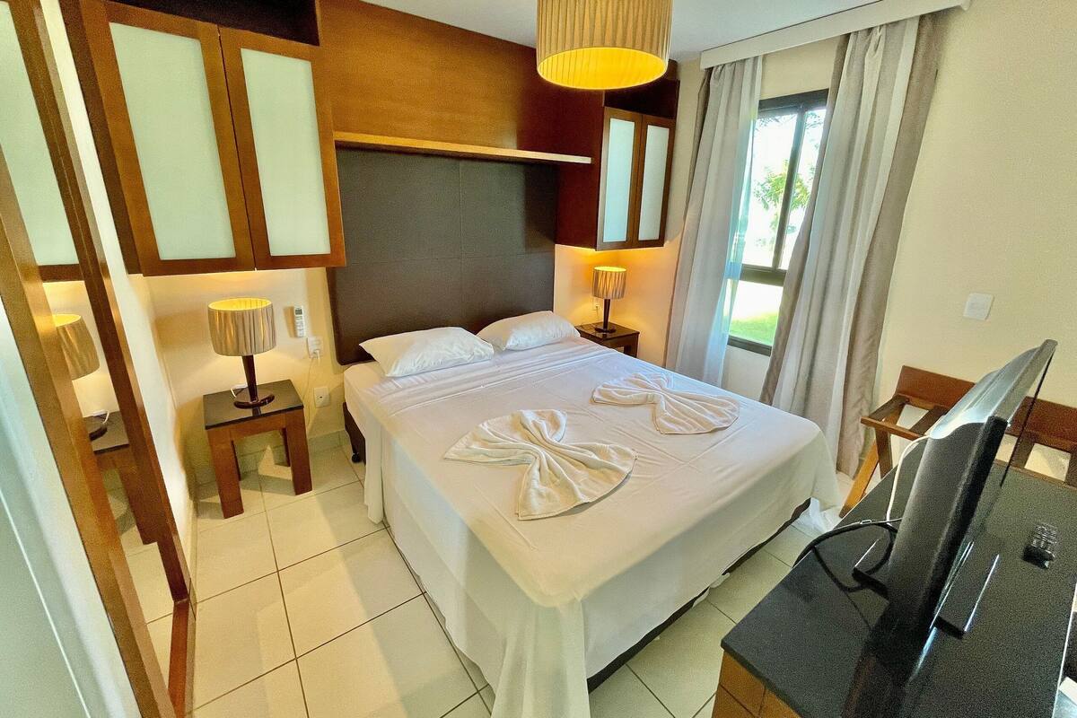 A hotel room with a bed, bedside lamps, a desk with a computer, and a window with curtains.