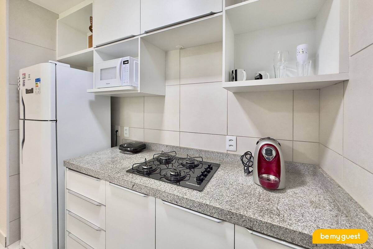 A kitchen with a refrigerator, microwave, stove, and kettle.