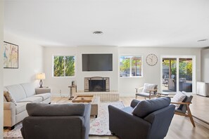 Ein modernes Wohnzimmer mit Kamin, Sitzgelegenheiten und großen Fenstern.