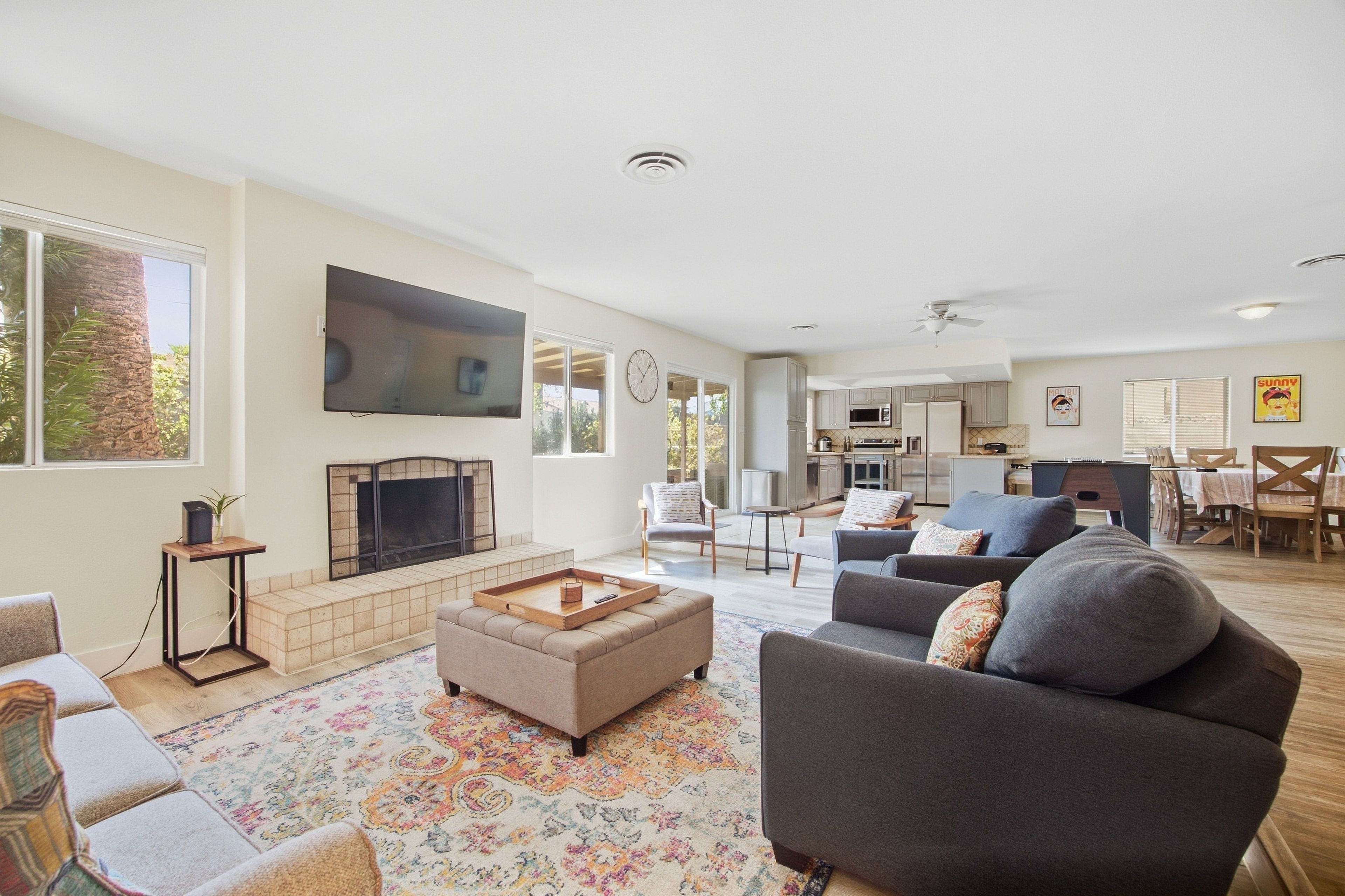 A spacious living room with a fireplace, a television, and a dining area with a kitchen in the background.