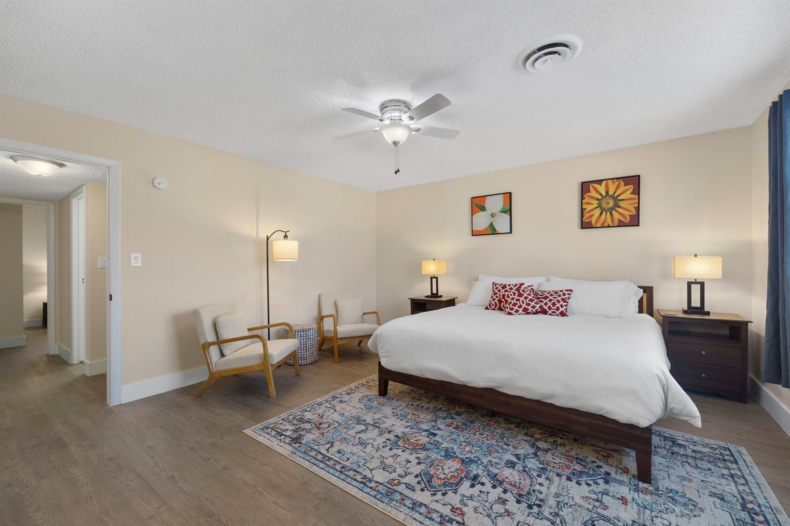 A bedroom with a bed, two bedside tables, a floor lamp, a ceiling fan, and a patterned rug.