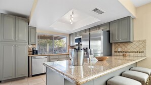 A modern kitchen with grey cabinets, a stainless steel refrigerator, a granite countertop, and bar stools. - Las Vegas Oasis with Private Pool and Hot Tub 12-min from The Strip (Las Vegas)