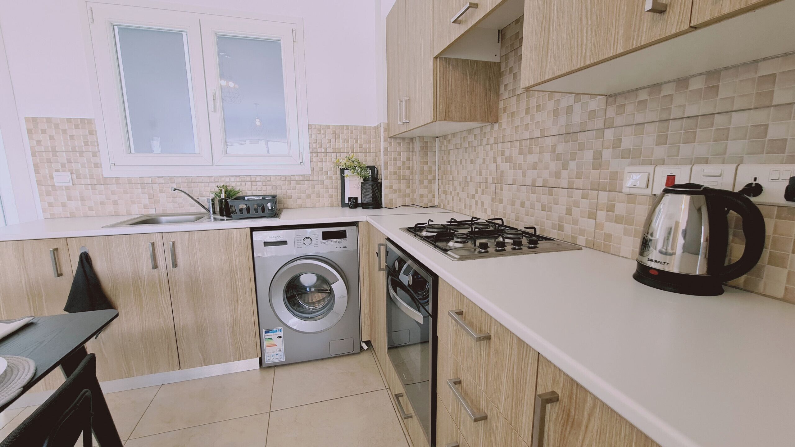 A compact kitchen with a washing machine, a stove, and a kettle.