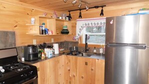 Una cocina compacta con armarios de madera, un refrigerador de acero inoxidable, una estufa a gas y una ventana con cortina.