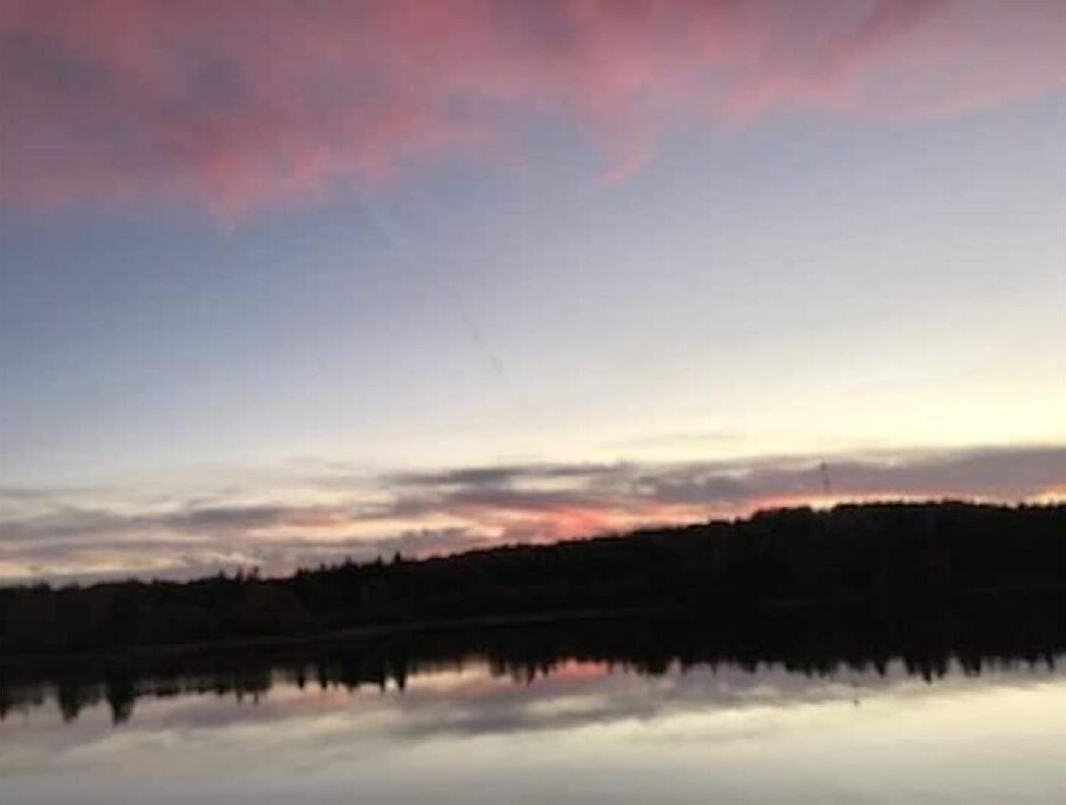 Un lac paisible au crépuscule, bordé d’une forêt et surplombé d’un ciel dégagé.