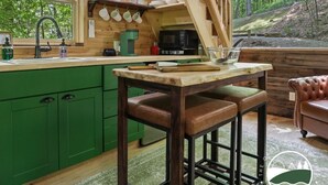 A cozy kitchen with a wooden staircase, green cabinets, and a view of the forest. - Rustic Treehouse Oasis in Hocking  Hills --Adventure Awaits (Logan)