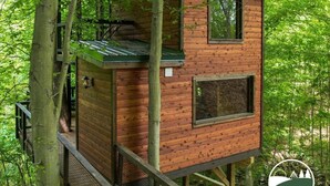 A wooden treehouse with a green roof, surrounded by lush greenery. - Rustic Treehouse Oasis in Hocking  Hills --Adventure Awaits (Logan)
