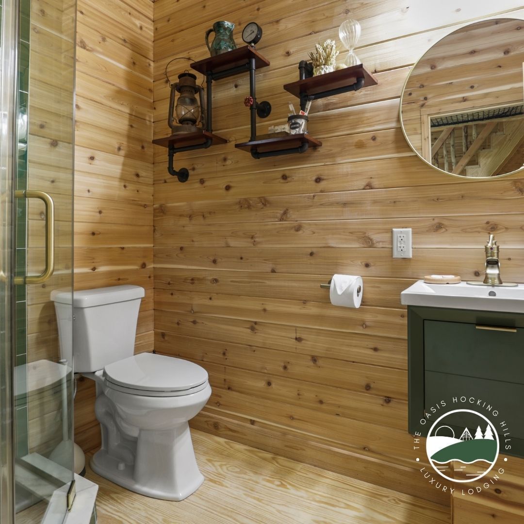 A wooden-paneled bathroom with a toilet, a sink, and shelves with decorative items.