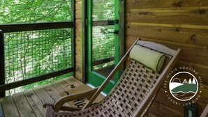 A wooden cabin with a green door, a hammock, and a view of trees through the window. - Rustic Treehouse Oasis in Hocking  Hills --Adventure Awaits (Logan)