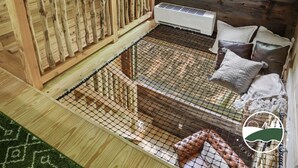 A wooden cabin with a loft bed, a window with a view of the forest, and a small heater on the wall. - Rustic Treehouse Oasis in Hocking  Hills --Adventure Awaits (Logan)