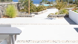 A patio with a white table and chairs, a stone wall, and a view of the sea. - VILLAS SCIROCCO (Santorini)