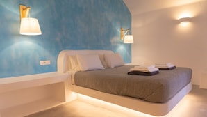 A modern bedroom with a bed, white nightstands, and blue walls. - VILLAS SCIROCCO (Santorini)
