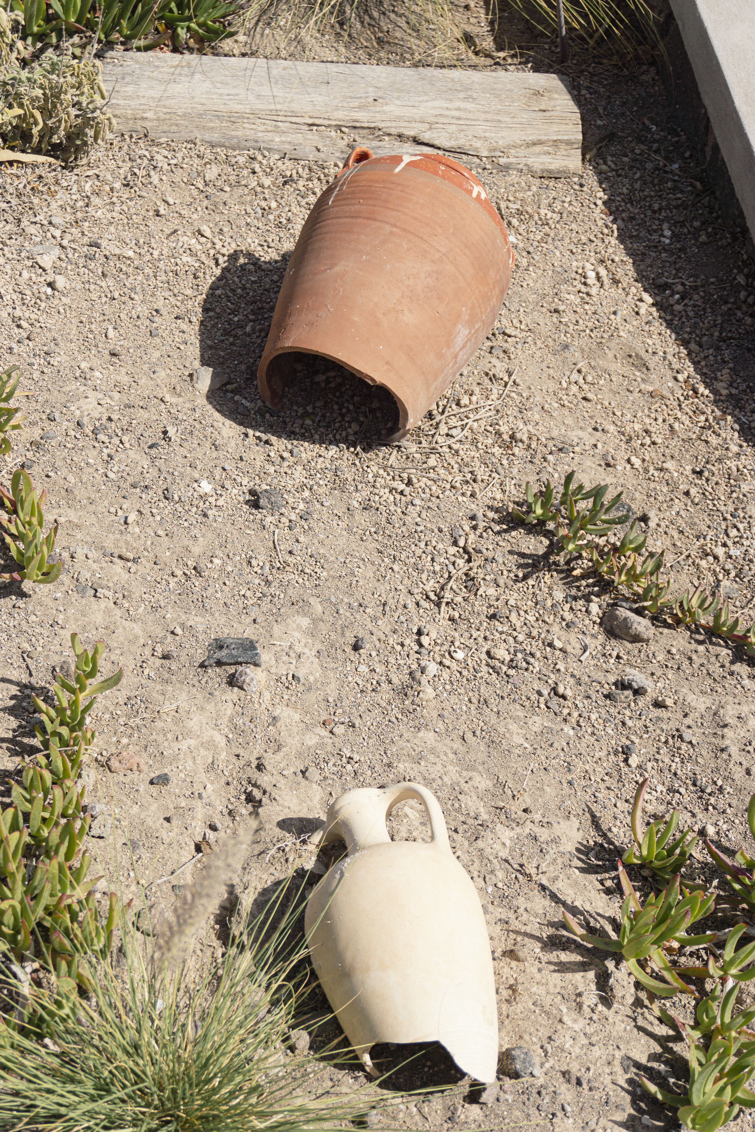 A terracotta pot and a white ceramic jug lying on a gravel surface.