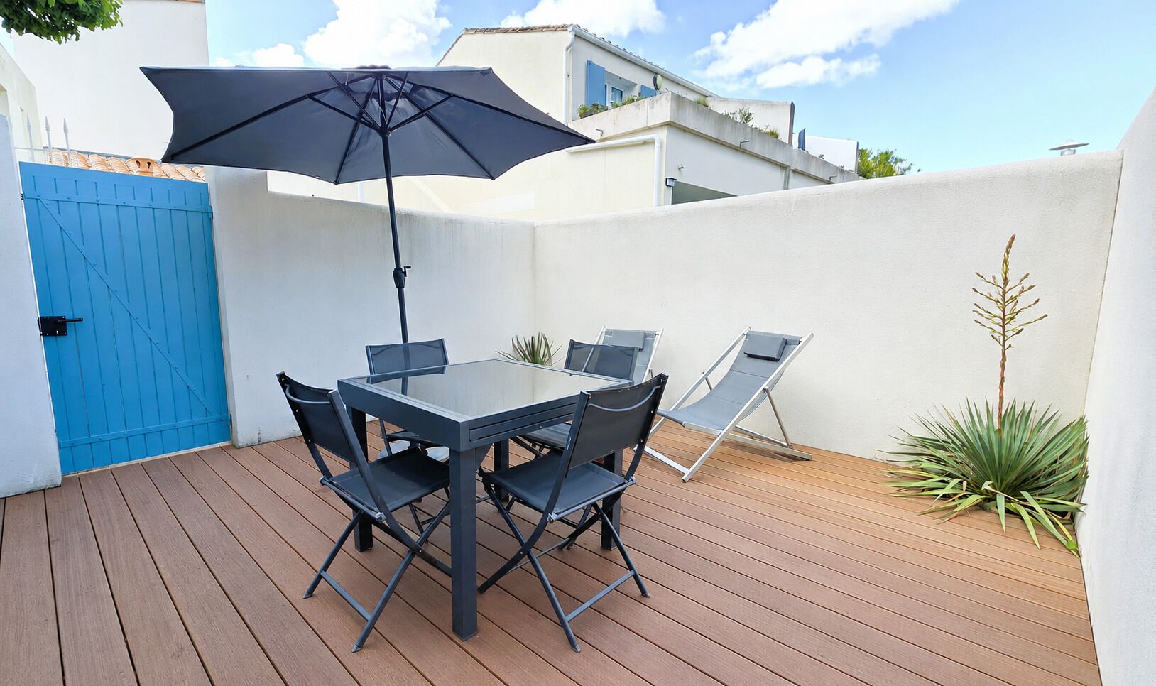 An outdoor patio with a table and chairs, a blue gate, and a potted plant.