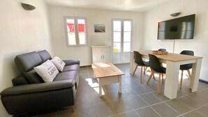 A modern living room with a black leather sofa, a wooden coffee table, and a dining area with a TV mounted on the wall. - AGATHE (2 route de St Martin, La Flotte) (La Flotte)