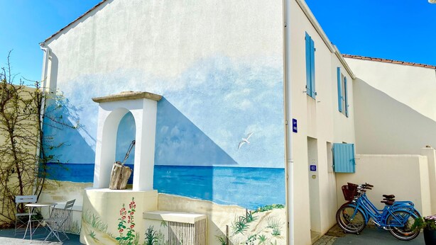 A building with a mural of the sea and sky, a bicycle, and outdoor seating. - AGATHE (2 route de St Martin, La Flotte) (La Flotte)