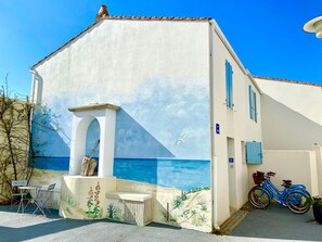 Un bâtiment orné d’une fresque représentant la mer et le ciel, avec un vélo et des sièges installés à l’extérieur.