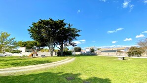 A grassy park area with a playground, a large tree, and a clear blue sky. - AGATHE (2 route de St Martin, La Flotte) (La Flotte)