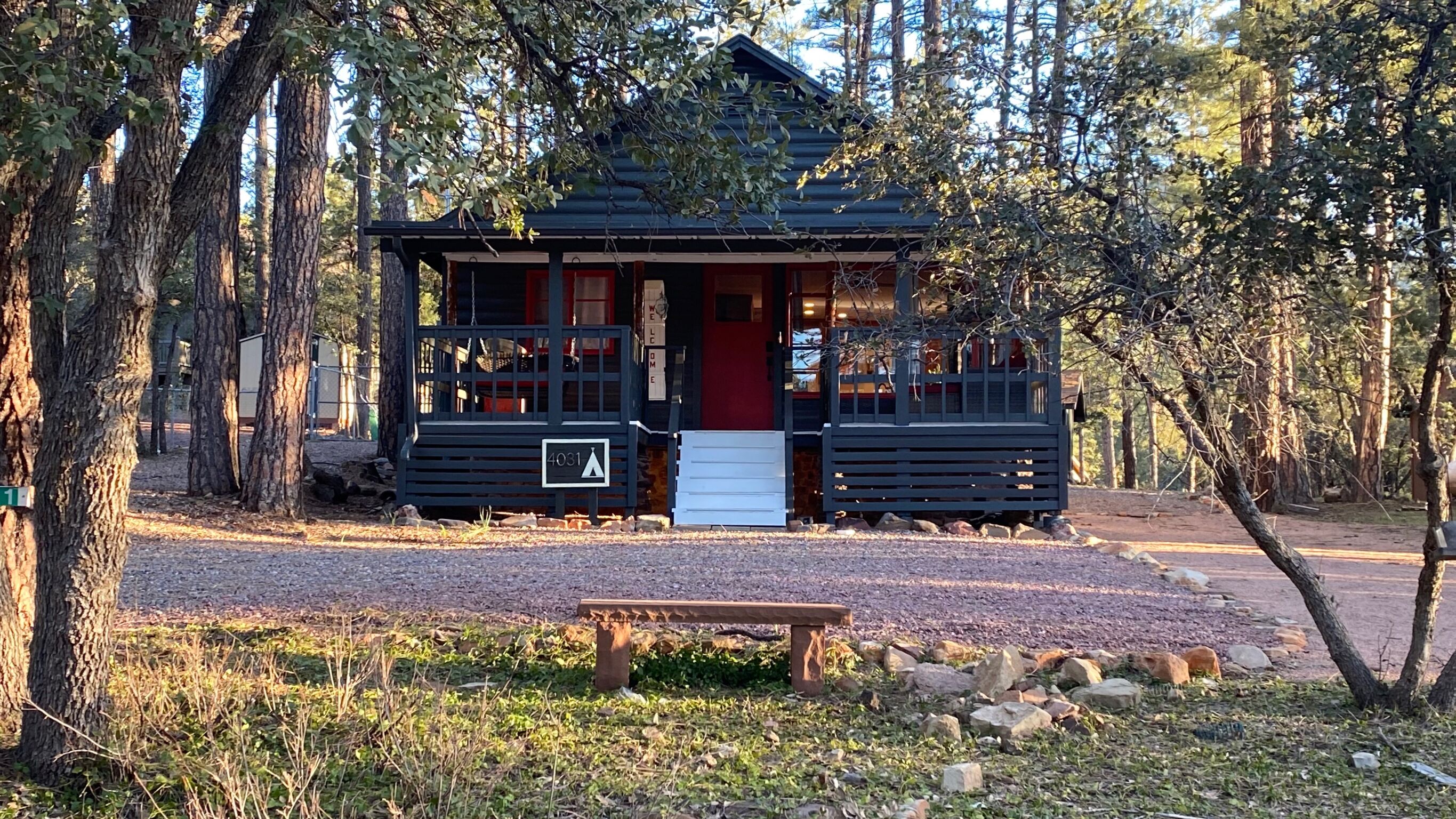Une cabane avec un porche à l’avant, un banc et une pancarte sur laquelle on peut lire : « BIENVENUE CHEZ VOUS ».