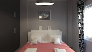 Quarto com cama, luminária pendente grande, quadro na parede e janela com cortinas.