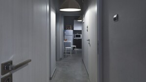 Um corredor estreito com uma porta à esquerda, uma cadeira branca e uma mesa ao centro.
