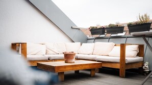 Un patio en la azotea con un conjunto de sofá de madera, una maceta de terracota y plantas en macetas en la barandilla.