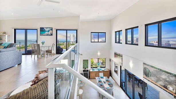 A spacious living area with a balcony, a dining area, and a staircase leading to an upper floor.