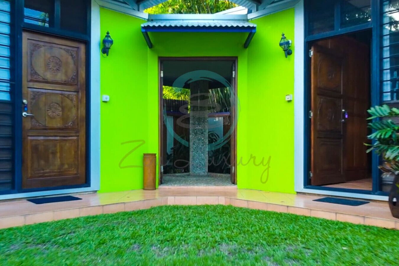 A building with a bright green facade, a wooden door with intricate carvings, and a small entrance with a glass door.