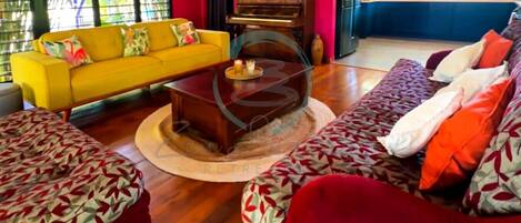 Una sala de estar con un sofá amarillo, un sofá rojo y una mesa de centro con superficie de vidrio.