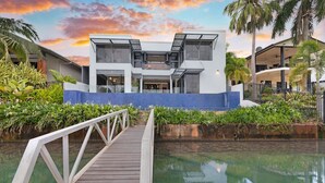 A modern hotel with a pool, a wooden bridge, and tropical plants.