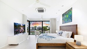 A modern hotel room with a large bed, a flat-screen TV, a wooden nightstand, and a view of the outdoors.