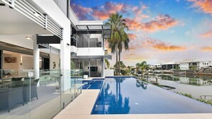 A modern building with a glass facade, a rooftop pool, and a view of a marina with boats.