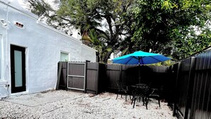 Un patio trasero con suelo de grava, una valla de madera y un paraguas azul.