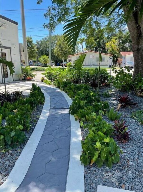 Un sendero curvo que conduce a un edificio de diseño moderno, rodeado de abundante vegetación y diversas plantas.