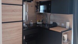 A modern kitchen with wooden cabinetry, a microwave, a sink, and a small countertop.