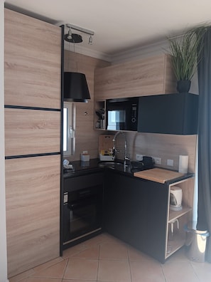 A modern kitchen with wooden cabinetry, a microwave, a sink, and a small countertop.