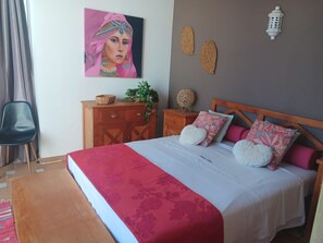 A bedroom with a bed, a wooden dresser, a chair, and a wall-mounted lamp.