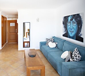 A living room with a blue sofa, patterned cushions, a wooden coffee table, and a large portrait on the wall.