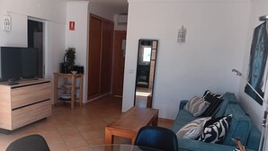 A living room with a TV, a sofa, a coffee table, and a dining area with chairs.