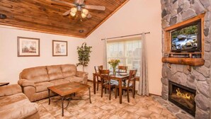A cozy living room with a stone fireplace, a ceiling fan, and a television mounted on the wall.
