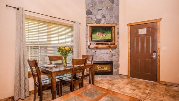 A dining area with a stone fireplace, a television mounted above it, and a wooden door to the right.