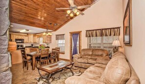 Un salón espacioso con techo de madera, un sofá de cuero, una zona de comedor con sillas de madera y una cocina al fondo.