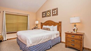 A hotel room with a bed, bedside tables, a lamp, and a window with blinds.
