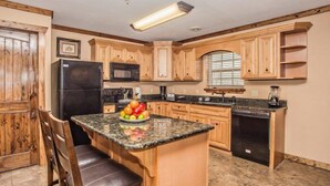 A kitchen with wooden cabinets, a black refrigerator, a microwave, a sink, and a fruit bowl on the counter.