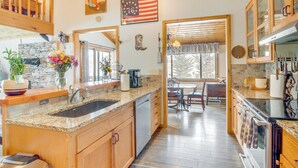 A kitchen with granite countertops, wooden cabinets, a built-in dishwasher, and a dining area with a view of the outdoors. - Fire Pit & Games! 10-Acre 'Majestic Mountain Home' (Thayne)