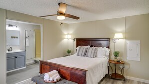 A bedroom with a bed, bedside lamps, a ceiling fan, a bedside table with a plant, and a bathroom with a sink and mirror. - Fire Pit + Deck: Peaceful Silver Creek Retreat (Silver Creek)