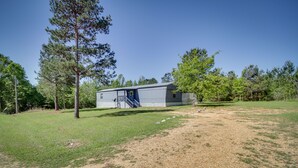 A single-story building with a covered outdoor area, surrounded by trees and grassy terrain. - Fire Pit + Deck: Peaceful Silver Creek Retreat (Silver Creek)